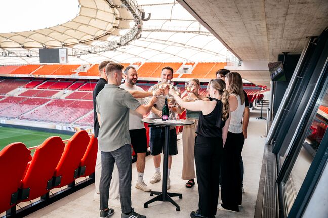 Mehrere Personen stehen um einen Tisch und stoßen mit einem Glas Champagner an 