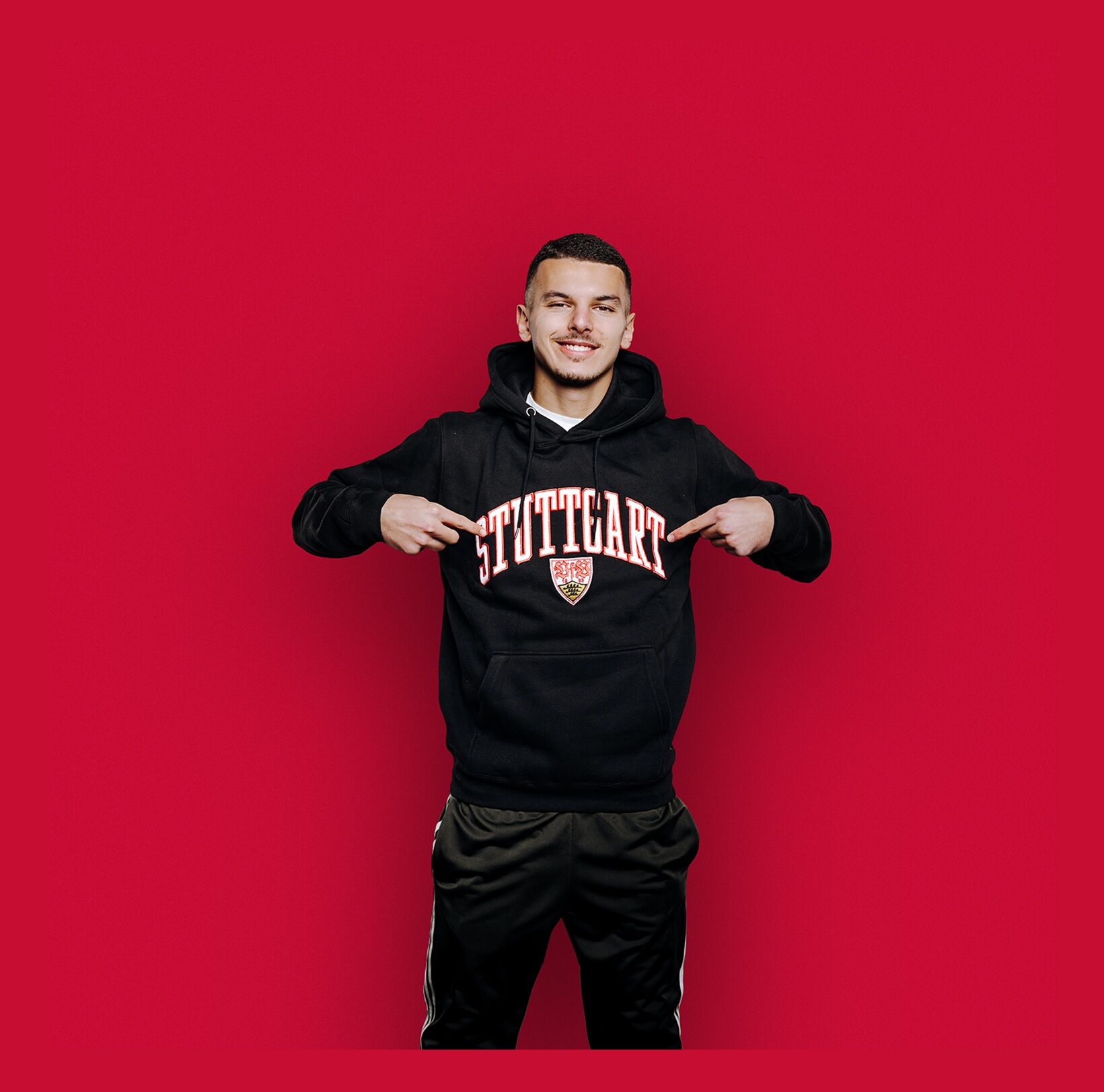 Spieler Bouanani trägt einen schwarzen VfB Hoodie mit großem Stuttgart Schriftzug und VfB Wappen 