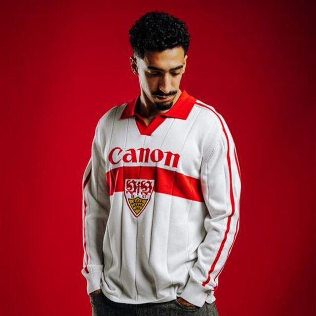 Tiago Tomas trägt das VfB Poloshirt Trikot Strick. Langarm Trikot in weiß mit rotem Brustring, rotem Polo-Kragen, großem VfB Wappen in der Mitte und Schriftzug Canon