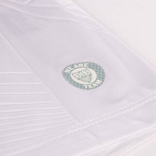 Nahaufnahme des silbernen runden VfB Wappens mit der Aufschrift We Are Team auf dem Heimtrikot 25/26