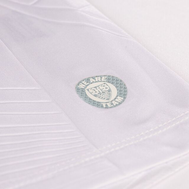 Nahaufnahme des silbernen runden VfB Wappens mit der Aufschrift We Are Team auf dem Heimtrikot 25/26