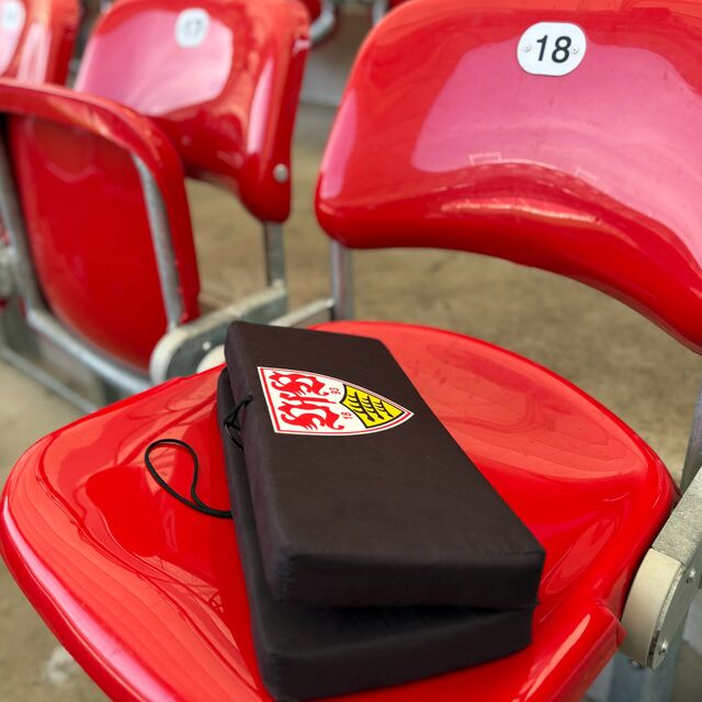 schwarzes Sitzkissen mit VfB Wappen liegt auf einem roten Stadionsitz