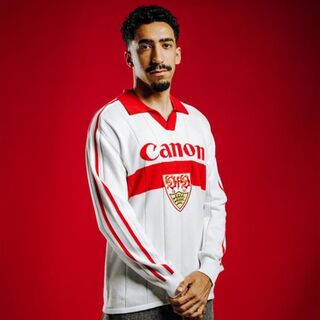 Tiago Tomas trägt das VfB Poloshirt Trikot Strick. Langarm Trikot in weiß mit rotem Brustring, rotem Polo-Kragen, großem VfB Wappen in der Mitte und Schriftzug Canon